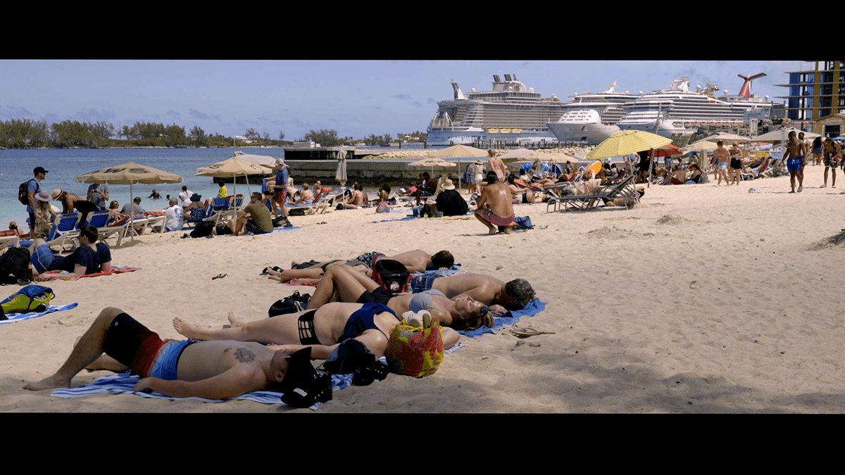 People on an overcrowded beach with a cruise liner in the background