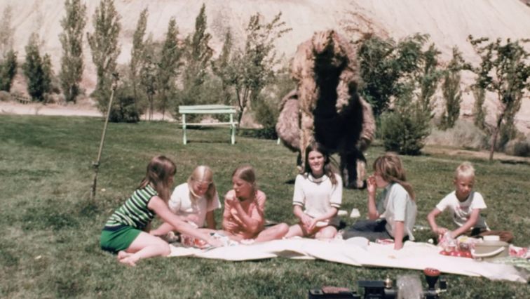 Children enjoying a picnic as the monster approaches behind them